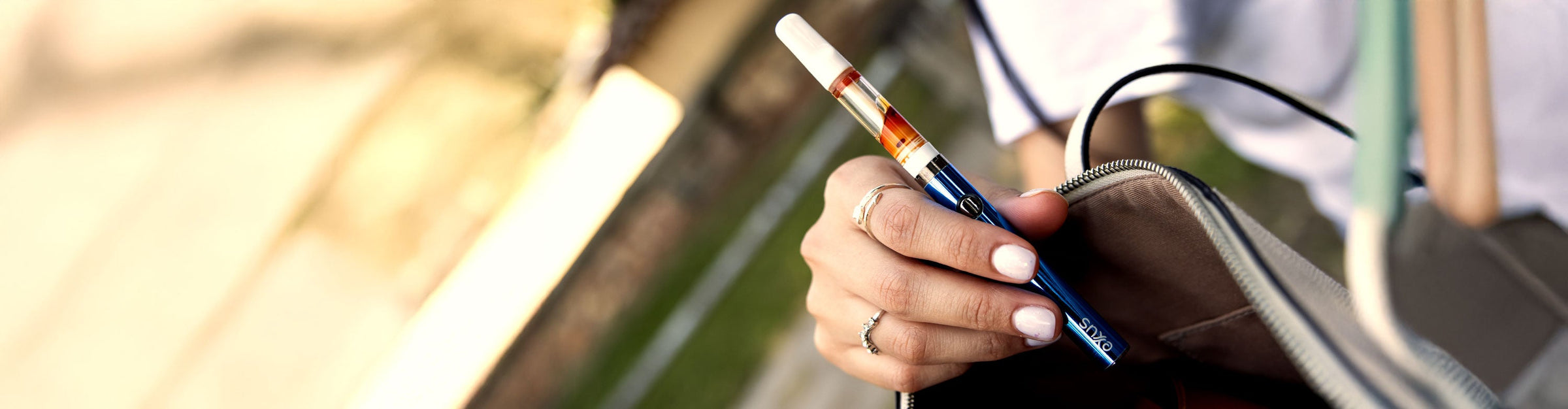 man holding a white Exxus Snap VV Mini portable Vaporizer outside near flower bush
